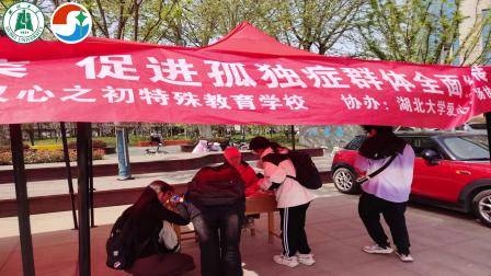 湖北大学爱心广场协会加入到关爱孤独症孩子的队伍中来-他们与心之初教育联合在户外开展了知识宣讲和手写祝福活动。为前来祝福人员绑上象征关爱孤独症人士的蓝色丝带